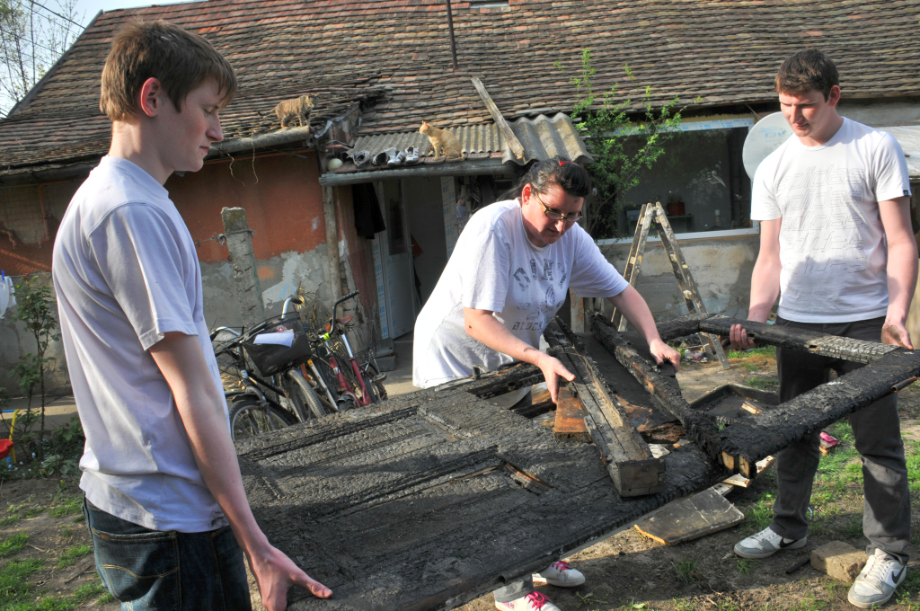 Az összeégett ajtót pakolja a család az udvaron. Tamás és Barnabás segít édesanyjának a romok eltakarításában (Fotó: Rajki Judit)